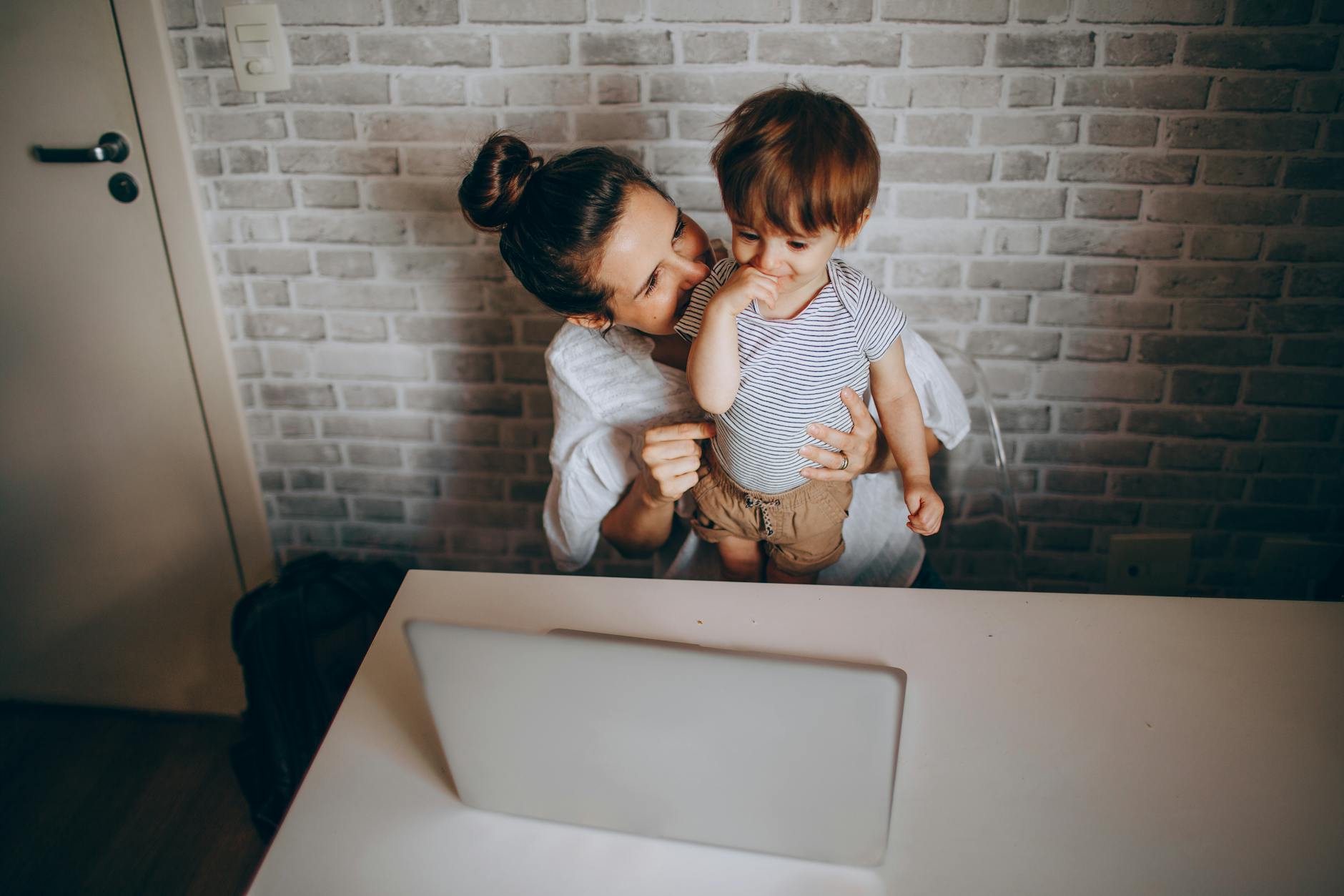 Mama rozmawia z małym dzieckiem przy laptopie w przytulnym mieszkaniu