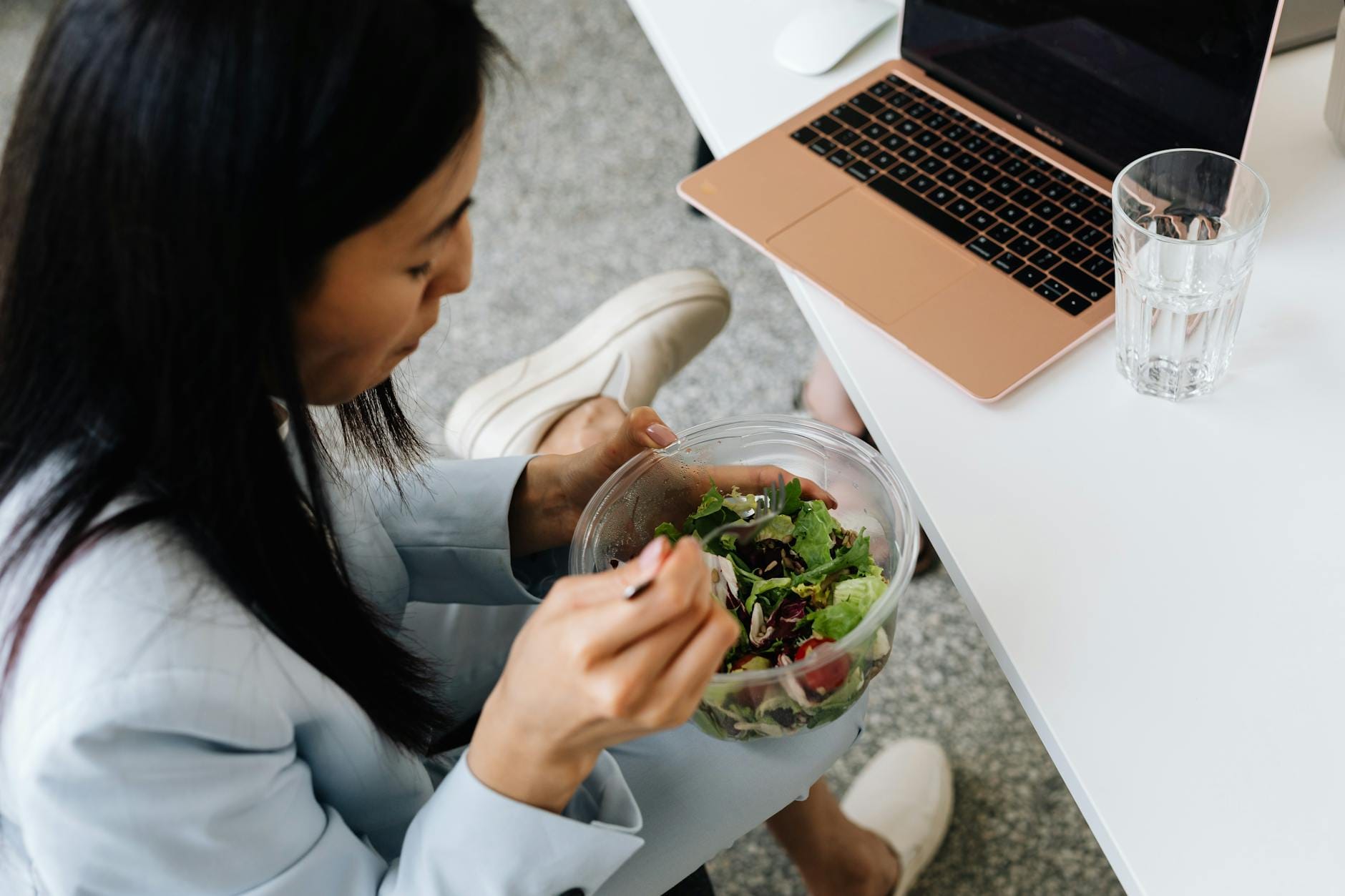 Kobieta je sałatkę przy biurku, obok otwarty laptop w pracy