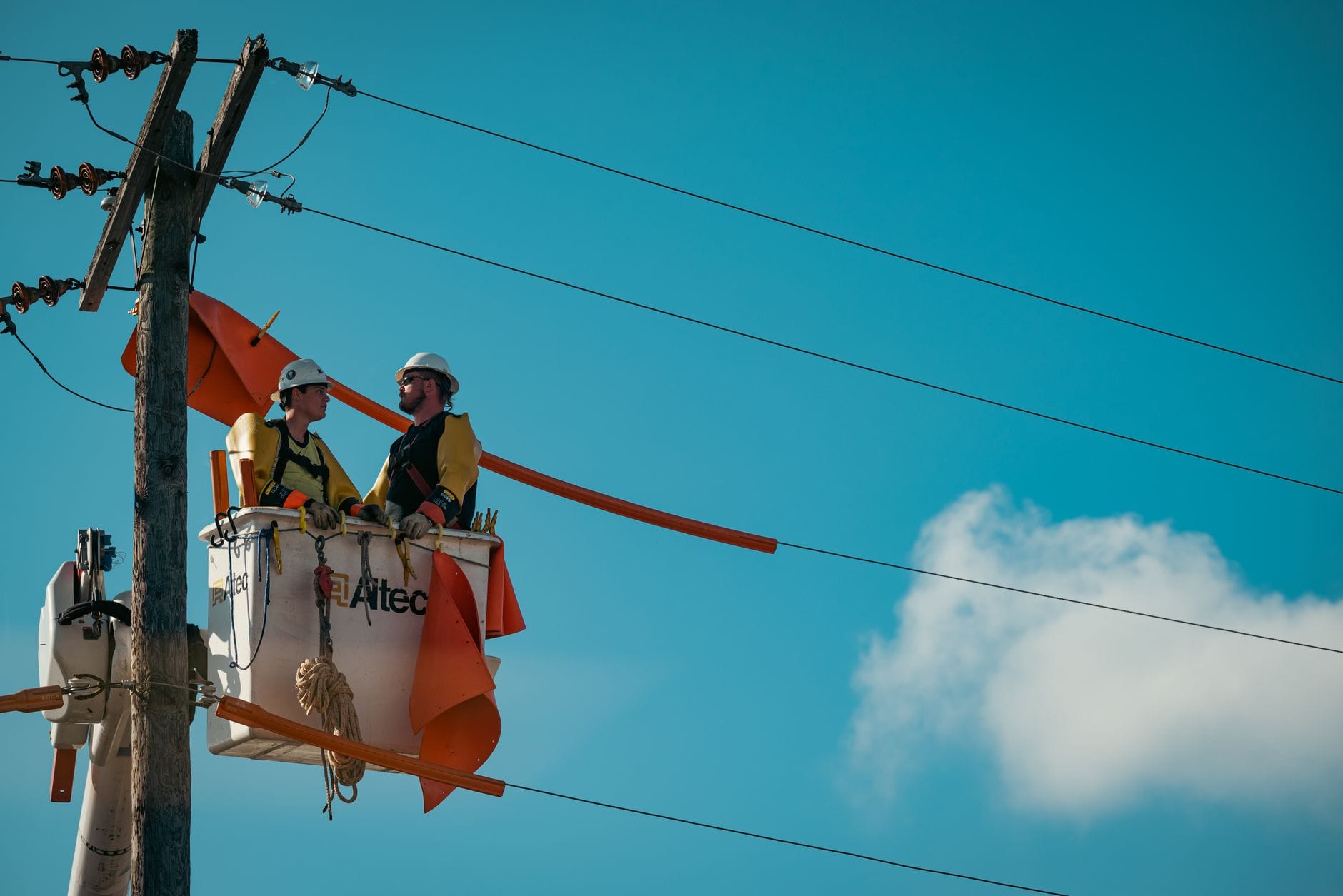 Elektrycy w uprzężach pracujący na słupie energetycznym na tle nieba