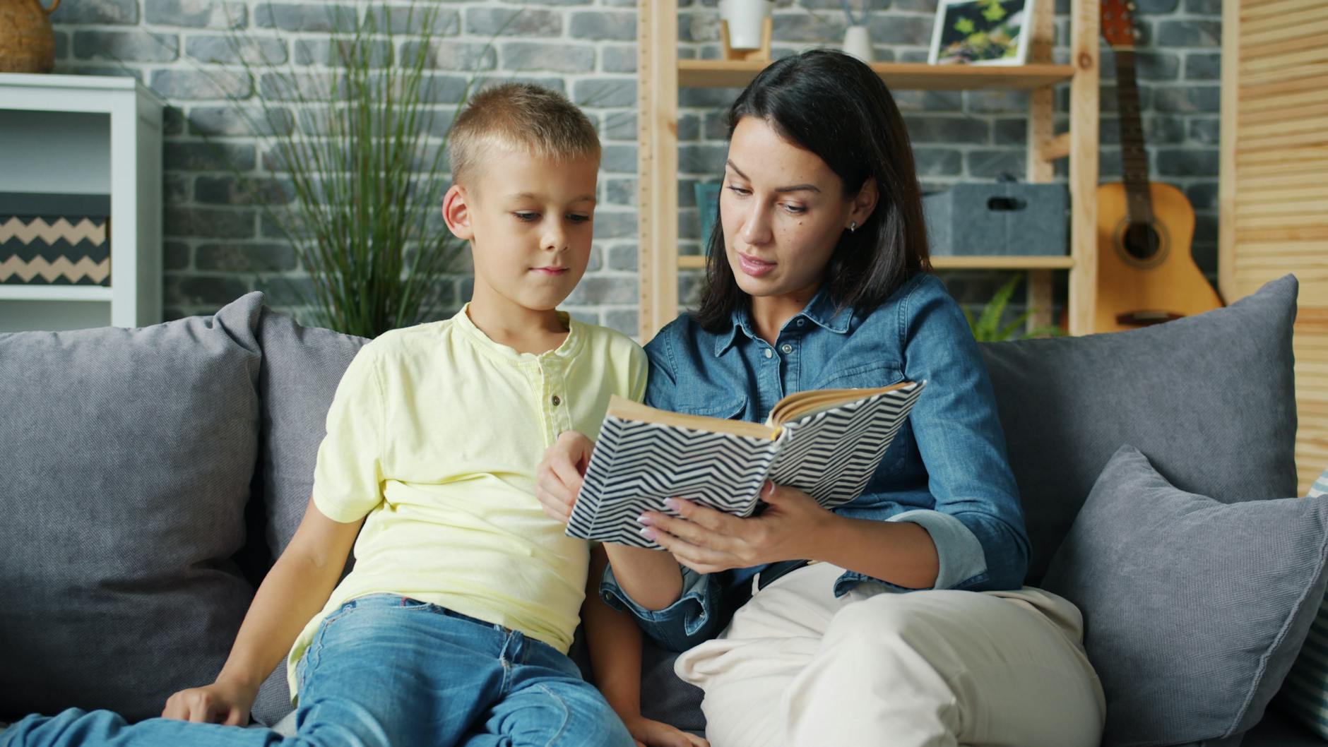 Mama czyta książkę z kilkuletnim synem na przytulnej kanapie