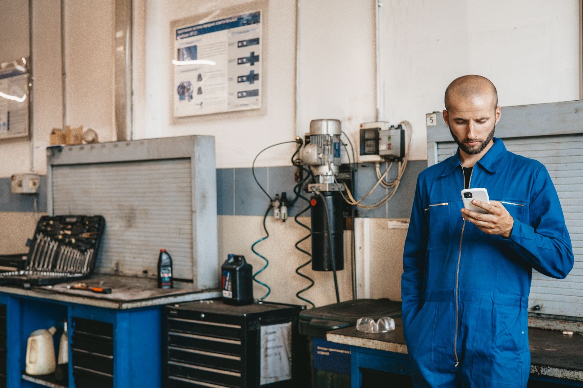 Mechanik w niebieskim kombinezonie korzysta ze smartfona w warsztacie